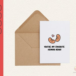 Puede incluir: Una tarjeta blanca con una linda ilustración de dos frijoles marrones con caras. Los frijoles se miran y tienen un corazón rosa encima. El texto en la tarjeta dice "¡Eres mi frijol humano favorito!"