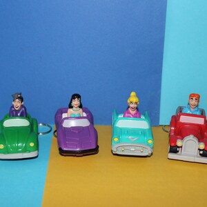 Op de afbeelding: Vier speelgoedauto's met figuren van mensen die ze besturen. De auto's zijn groen, paars, blauw en rood. De figuren dragen verschillende gekleurde kleding.