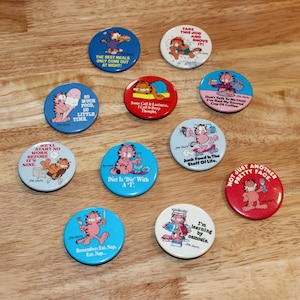 May include: A collection of Garfield the cat pinback buttons in various colors. Each button features Garfield with humorous phrases like "Diet Is 'Die' With A 'T'" and "I'm learning by osmosis."