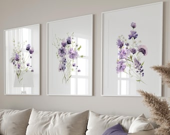 May include: A white sectional sofa with three cushions, two in a light purple colour and one in a darker purple colour. The sofa is in a living room with a light beige wall and three framed watercolour paintings of purple flowers. A round wooden coffee table sits in front of the sofa.