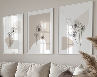 May include: A white sectional sofa with brown throw pillows in a living room with a beige wall and three framed prints of dandelion flowers. The room also features a brown floor, a round coffee table, a gray ottoman, a floor lamp, and a vase with dried pampas grass.
