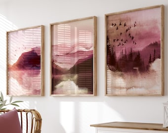 May include: Three framed wall art prints featuring watercolor landscapes in shades of dusty rose, burgundy, and cream. The artwork depicts mountain silhouettes, pine forests, and flocks of birds in flight, all encased in light-toned wooden frames.