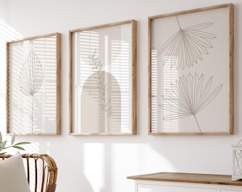 May include: A white cabinet with two drawers and two doors, a wicker chair with a white throw blanket, a woven basket, and three framed prints with line drawings of palm leaves on a white wall.