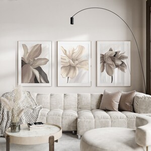May include: Three framed prints of beige and brown floral illustrations. The prints are hung on a white wall above a white sectional sofa with beige throw pillows.