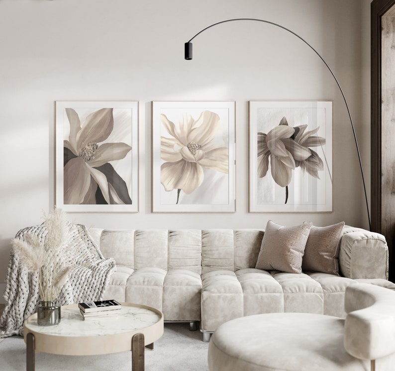 May include: Three framed prints of beige and brown floral illustrations. The prints are hung on a white wall above a white sectional sofa with beige throw pillows.