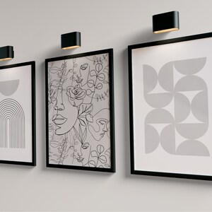 May include: Three black framed prints with white backgrounds and black line drawings. The left print features a half circle and a series of lines forming an arch. The center print features a pattern of overlapping faces and flowers. The right print features a pattern of overlapping semi-circles.