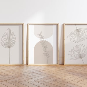 Puede incluir: Tres cuadros de pared con dibujos lineales de hojas bot&aacute;nicas en tinta marr&oacute;n sobre un fondo beige claro. La l&aacute;mina central incluye dos formas de arco superpuestas en un tono bronceado suave detr&aacute;s de una ilustraci&oacute;n de una hoja de helecho.