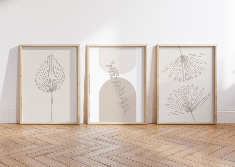 Puede incluir: Tres cuadros de pared con dibujos lineales de hojas bot&aacute;nicas en tinta marr&oacute;n sobre un fondo beige claro. La l&aacute;mina central incluye dos formas de arco superpuestas en un tono bronceado suave detr&aacute;s de una ilustraci&oacute;n de una hoja de helecho.
