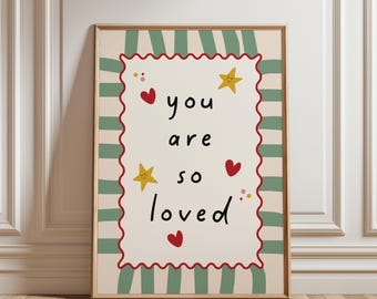 May include: A rectangular wall art print featuring the text you are so loved in black lettering. The design includes a scalloped red border, yellow stars with faces, and red hearts on a cream background, framed by green and cream vertical stripes.
