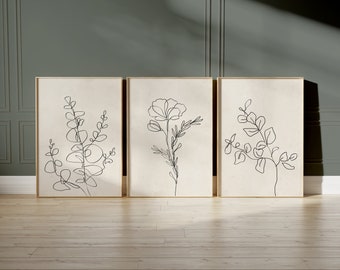 May include: Three minimalist line art prints featuring botanical illustrations. The prints are framed in a light wood frame and are displayed on a light wood floor against a green wall.