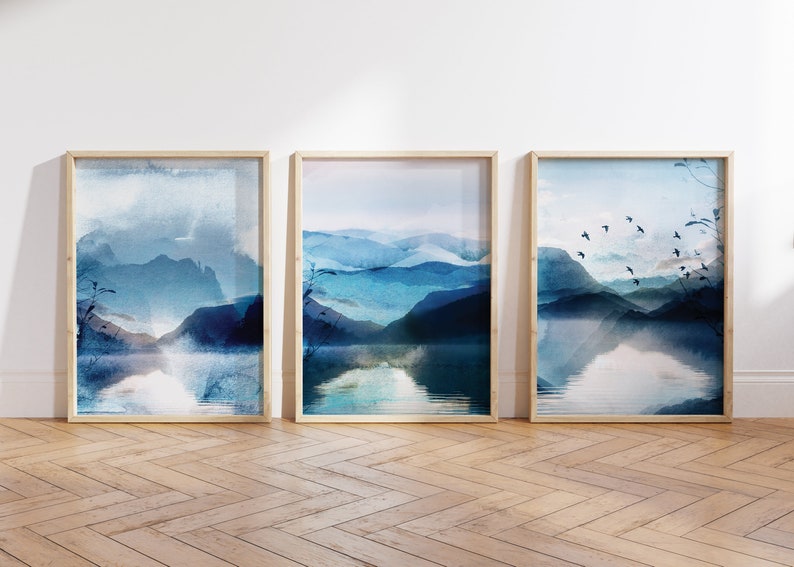 set of 3 vibrant blue watercolour abstract landscape wall art prints featuring a lake, mountains, trees and birds in flight in the distance