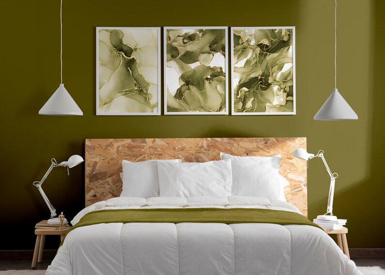 May include: A white bed with a green duvet cover and two white pillows. The headboard is made of wood and has a natural finish. There are three framed abstract paintings above the headboard, each with a green and gold design. Two white pendant lights hang from the ceiling.