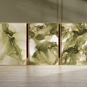 May include: Three framed abstract art prints with green and gold swirling patterns. The prints are in gold frames and are hanging on a wall.