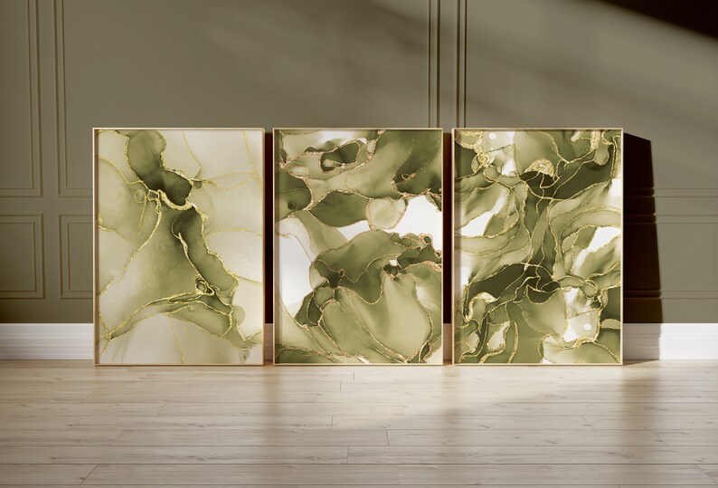 May include: Three framed abstract art prints with green and gold swirling patterns. The prints are in gold frames and are hanging on a wall.