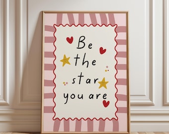 May include: A rectangular wall art print featuring a cream-colored center with a red scalloped border. The text reads "Be the star you are" in black, surrounded by yellow stars and red hearts on a background of vertical pink stripes.