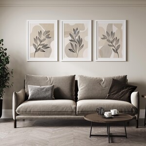 Three beige-toned wall art prints featuring minimalist line drawings of leaves on a textured watercolour background. The prints are arranged in a triptych format, creating a cohesive and stylish look.  Each print showcases a similar leaf motif, but with subtle variations in composition and placement. The neutral color palette and organic forms create a serene and sophisticated aesthetic, suitable for modern or minimalist interior design