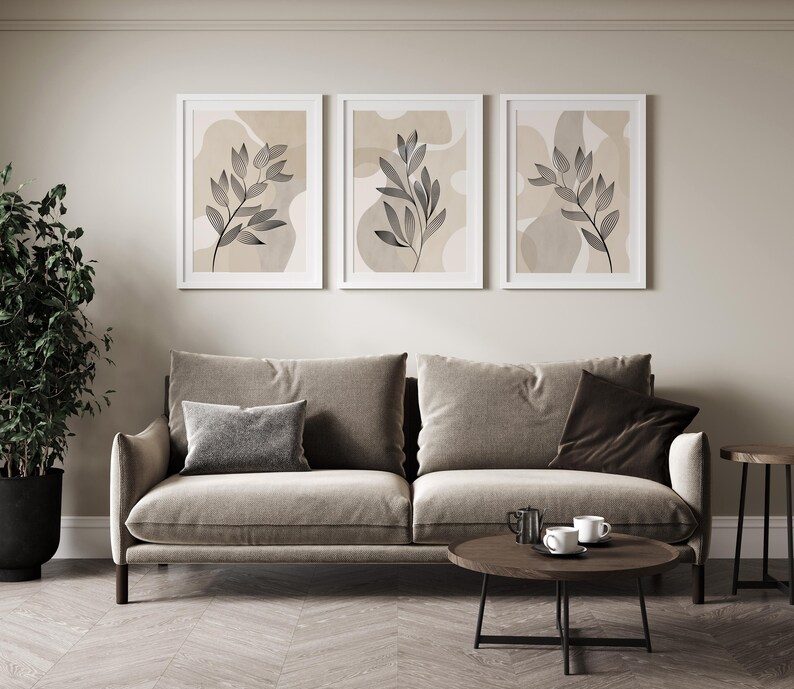 Three beige-toned wall art prints featuring minimalist line drawings of leaves on a textured watercolour background. The prints are arranged in a triptych format, creating a cohesive and stylish look.  Each print showcases a similar leaf motif, but with subtle variations in composition and placement. The neutral color palette and organic forms create a serene and sophisticated aesthetic, suitable for modern or minimalist interior design