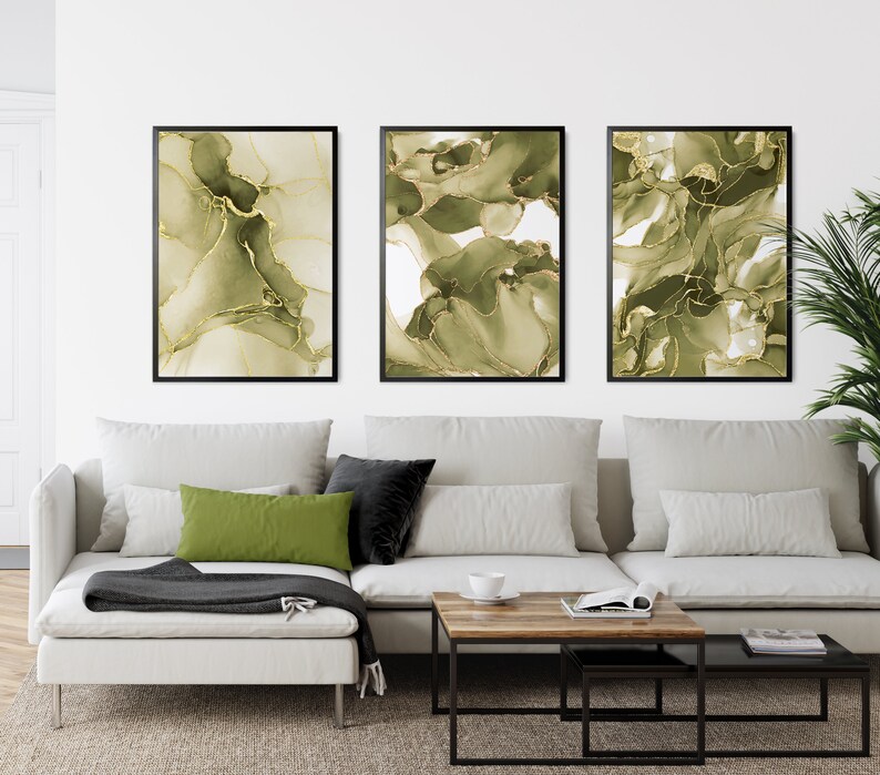 May include: Three framed abstract art prints with green and gold swirling patterns. The prints are hung on a white wall above a white sectional sofa with green and black throw pillows.