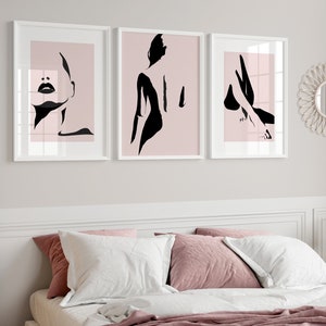 May include: Three framed wall art prints featuring black minimalist silhouettes of a human figure against a soft pink background. The first print shows a face, the second a back profile, and the third a leg, all displayed in white frames.