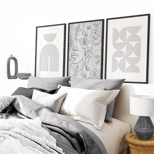 May include: Three black framed prints with abstract line art designs. The prints are hanging on a white wall above a gray bed with white pillows and a white blanket.