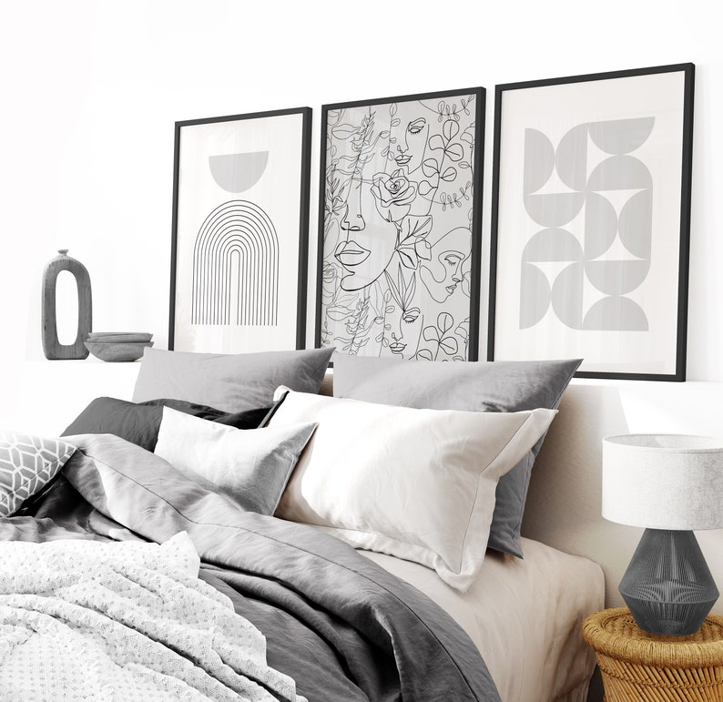 May include: Three black framed prints with abstract line art designs. The prints are hanging on a white wall above a gray bed with white pillows and a white blanket.