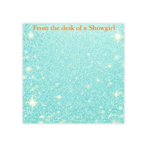 May include: A square notepad with a turquoise glitter background and sparkling accents. The text "From the desk of a Showgirl" is printed in orange at the top. The notepad is blank and ready for notes.