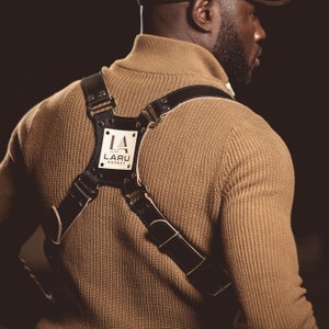 May include: A brown sweater with a black leather harness featuring a white rectangular tag with the text "LA LARU AGENCY".
