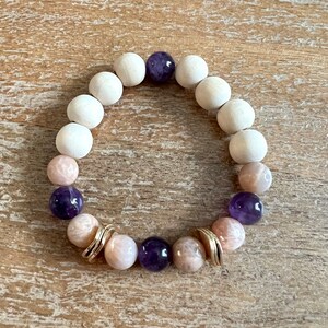 May include: A bracelet made with natural wood beads, amethyst, and sunstone beads. The bracelet has gold accents.