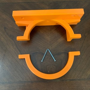 May include: Bright orange 3D-printed shelf bracket set. The set includes a top piece with mounting holes, a curved support, and a bottom piece. Two silver screws are included for assembly. The pieces are made of plastic.
