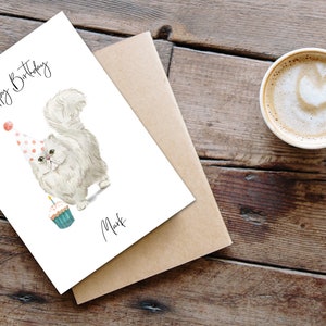 Puede incluir: Una tarjeta de cumplea&ntilde;os blanca con un gato blanco que lleva un gorro de fiesta de lunares rosa y blanco y sostiene un cupcake con una vela encendida. La tarjeta dice "Feliz cumplea&ntilde;os" y "Mark".