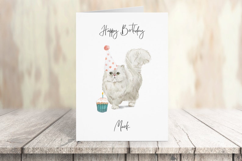 Puede incluir: Un gato blanco con un gorro de fiesta de lunares rosa y blanco y sosteniendo un cupcake con una vela encendida. El texto "Happy Birthday Mark" est&aacute; escrito en la tarjeta.