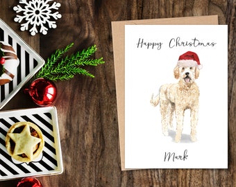 Könnte beinhalten: Weihnachtskarte mit einer Aquarellillustration eines Golden Doodle mit Weihnachtsmütze. Die Karte trägt die Aufschrift "Happy Christmas" über dem Hund und "Mark" darunter. Die Karte liegt auf einer Holzoberfläche mit festlicher Dekoration.
