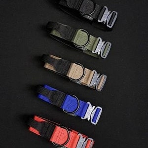 Pode incluir: Cinco coleiras para cães em várias cores: preto, verde camuflado, bege camuflado, azul e vermelho. Cada coleira apresenta uma tira preta, um anel em D de metal e uma fivela de metal prateado. As coleiras estão dispostas verticalmente sobre um fundo preto.