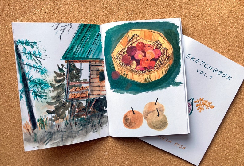 May include: An open sketchbook with watercolor illustrations. The left page shows a small wooden cabin with a green roof in a forest setting. The right page shows a basket of red apples and three pears on a green background. The cover of the sketchbook says "Sketchbook Vol. 1" with a small illustration of a leaf.