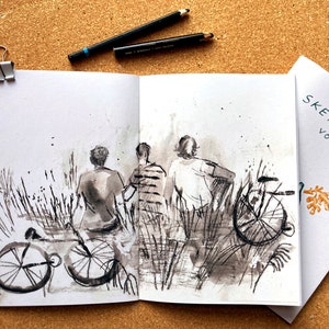 May include: A black and white ink drawing of three people standing in a field of tall grass. They are looking at something in the distance. There are two bicycles in the foreground. The drawing is in a sketchbook with the text "SKETCHBOOK VOL. 1" on the cover.