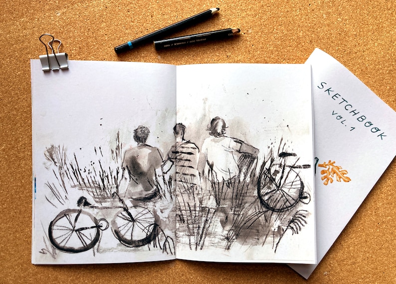 May include: A black and white ink drawing of three people standing in a field of tall grass. They are looking at something in the distance. There are two bicycles in the foreground. The drawing is in a sketchbook with the text "SKETCHBOOK VOL. 1" on the cover.