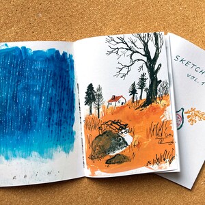May include: An open sketchbook with a blue watercolor painting of rain on the left page and a watercolor painting of a house in a forest on the right page. The cover of the sketchbook is white with the text "SKETCHBOOK VOL. 1" in black.