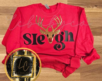 May include: Red long-sleeved sweatshirt with a black graphic of the word "Sleigh" and a gold sequin reindeer with a red nose.