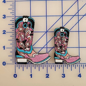 May include: Two embroidered pink cowboy boot patches with black, white, and blue accents. The larger boot is 2 inches tall and the smaller boot is 1.5 inches tall.