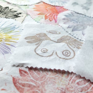 Op de afbeelding: Een verzameling stoffen vierkanten met verschillende gedrukte ontwerpen, waaronder bloemenpatronen, abstracte vormen en een ontwerp van twee handen met vleugels en een hartvorm.