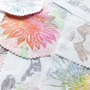 Peut inclure: Une collection de cercles en tissu avec différents motifs imprimés à la main. Les motifs comprennent une grande fleur orange et rose, une fleur verte et bleue et un motif floral noir et blanc.