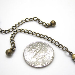 Peut inclure: Un extenseur de cha&icirc;ne en bronze avec deux petites perles rondes et un fermoir &agrave; ressort. La cha&icirc;ne est &agrave; peu pr&egrave;s de la taille d'une pi&egrave;ce de dix centimes d'euro.