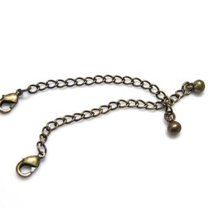 Peut inclure: Un extenseur de cha&icirc;ne en bronze avec deux fermoirs mousqueton et deux perles rondes.