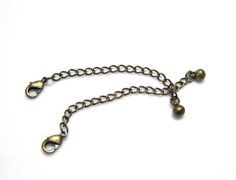 Peut inclure: Un extenseur de cha&icirc;ne en bronze avec deux fermoirs mousqueton et deux perles rondes.