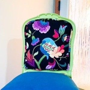 May include: A green painted chair with a blue velvet seat and a floral patterned cushion. The chair has a carved wooden frame and sits on a tiled floor.