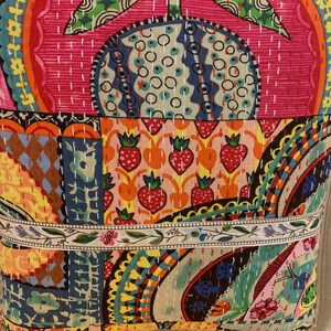 May include: A colorful patchwork chair cushion with a floral and geometric pattern. The cushion is made of different fabrics sewn together and has a white trim.