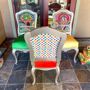 May include: Three ornate chairs with silver frames and colorful patterned upholstery. The chair in the center has a white and multi-colored polka dot pattern. The chairs are on a tiled floor with a yellow ceramic frog figurine.