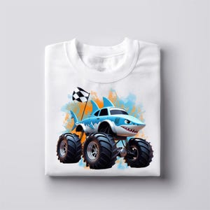 Peut inclure: T-shirt blanc avec un motif bleu et orange d'un camion monstre requin. Le camion a de grandes roues noires et un drapeau &agrave; damier.