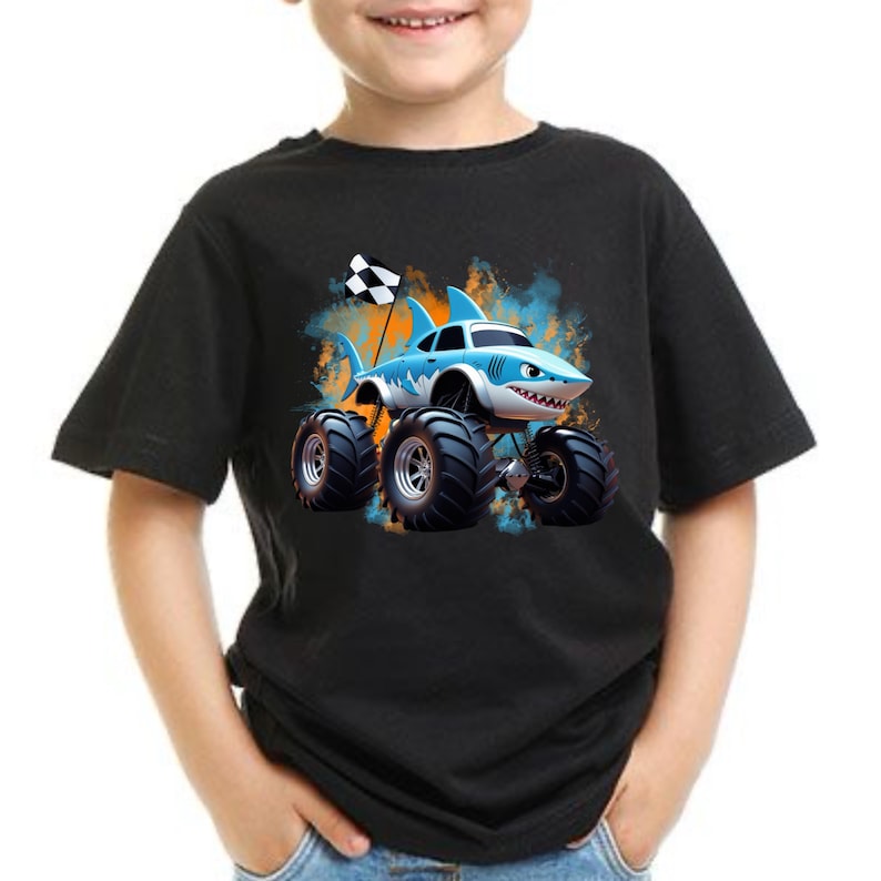 Peut inclure: Un t-shirt noir avec un camion monstre de dessin anim&eacute; bleu et blanc avec des nageoires de requin et un drapeau &agrave; damier. Le camion roule &agrave; travers une &eacute;claboussure de peinture orange et bleue.