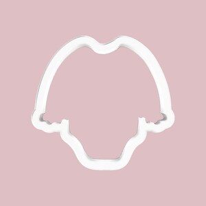 K&ouml;nnte beinhalten: Ein wei&szlig;er Ausstecher aus Kunststoff in Form eines Baby-Stramplers. Der Ausstecher hat eine abgerundete Oberseite und eine gebogene Unterseite. Der Hintergrund ist einfarbig hellrosa.